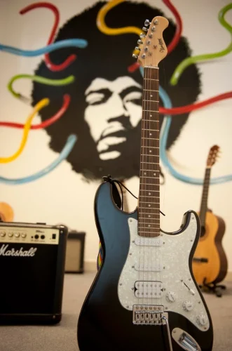 Im Vordergrund eine E-Gitarre, im Hintergrund eine Wandbemalung mit Jimi Hendrix.