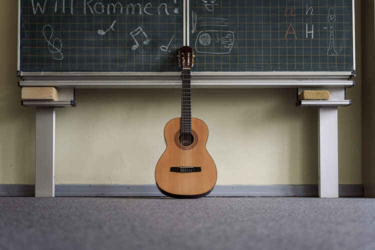 Eine Akustikgitarre zentriert im Bild an eine Schultafel gelehnt.