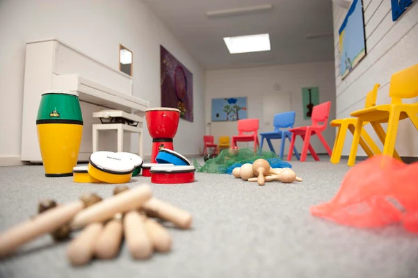 Ein Klassenzimmer mit Teppich und bunten Stühlen in dem verschiedene Musikinstrumente für Kinder auf dem Boden liegen.